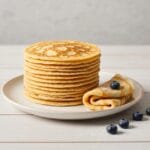Recette crepe facile : 5 étapes pour réussir Pile de crêpes dorées et moelleuses avec des myrtilles sur une assiette en céramique, illustrant une recette crepe facile.