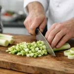 Cuisson poireaux: Mains de chef coupant des poireaux frais sur une planche en bois. Préparation professionnelle pour vos rece