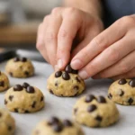 La recette des cookies facile en 5 étapes pour un résultat parfait à Des mains ajoutent des pépites de chocolat à la pâte pour une recette des cookies facile et parfaite sur une plaque.