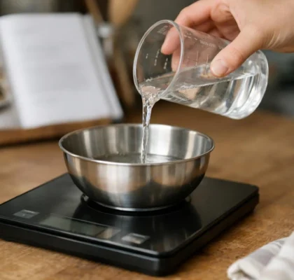 "Femme qui utilise une balance de cuisine pour convertir des centilitres en grammes, avec un verre doseur et un livre de rece