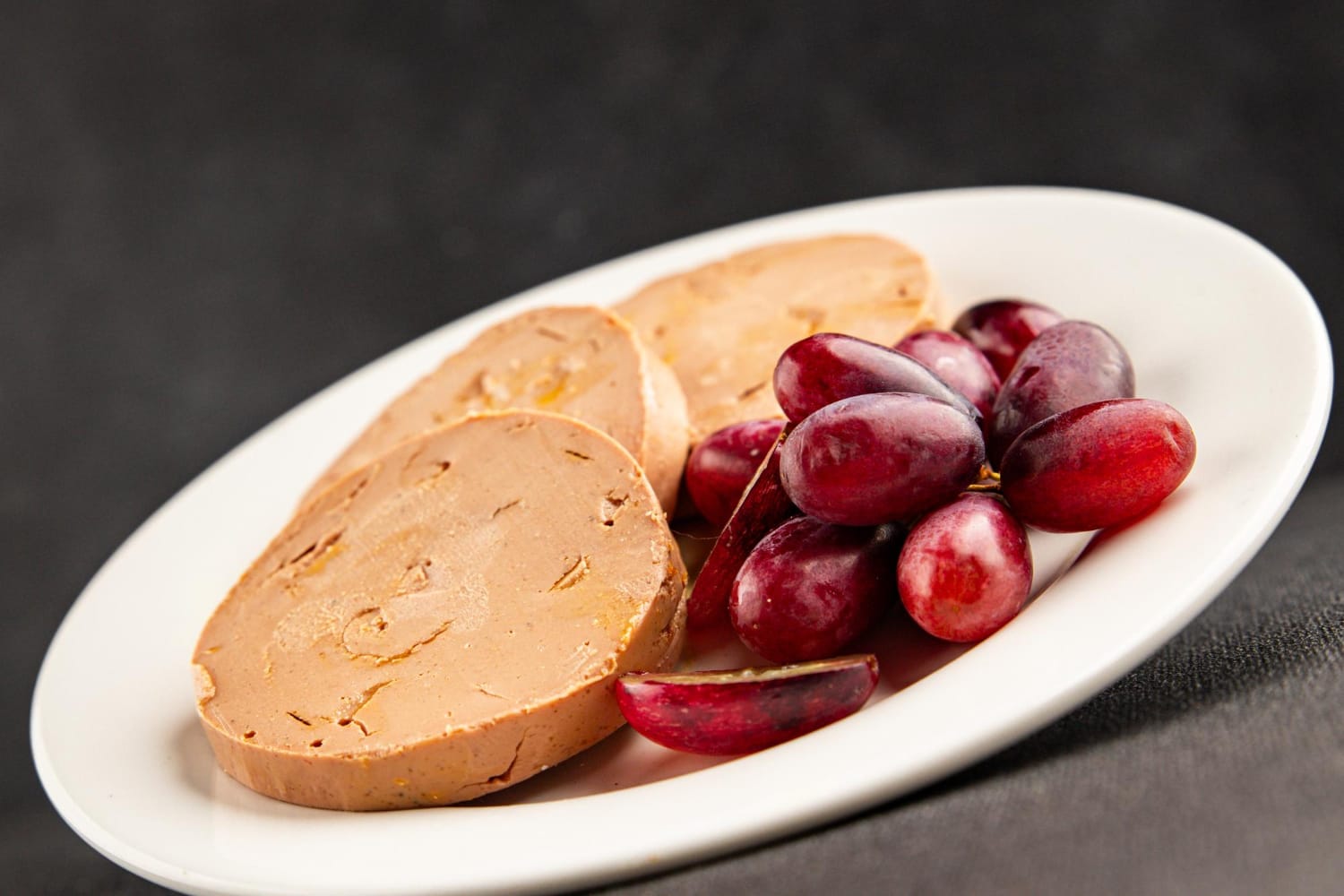 Foie gras : comment composer une assiette élégante et équilibrée ? Mets gastronomique frais et délicieux composé de foie gras, sur fond rustique avec une table noire.